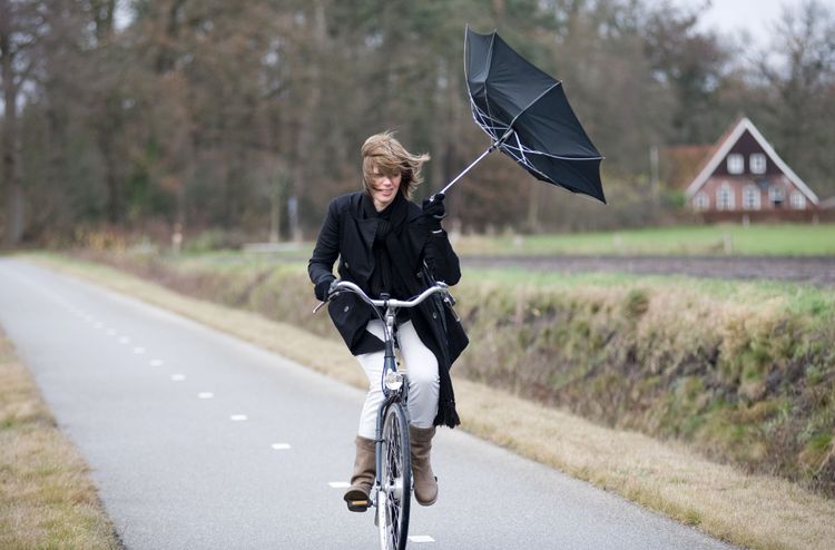 Kvinde der cykler på en cykelsti med en paraply der vender forkert på grund af kraftig vind