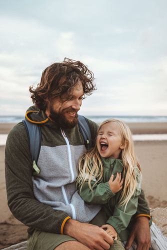 Far og datter der sidder på en strand med vind i håret